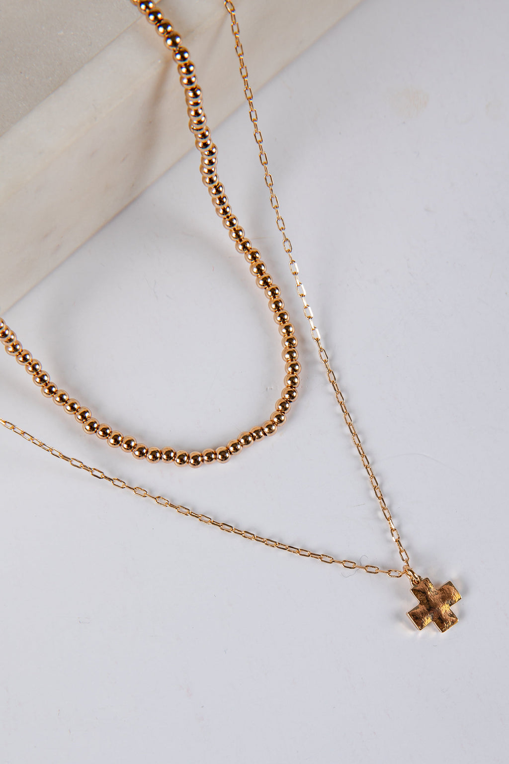 Two gold necklaces with a cross pendant on a light background