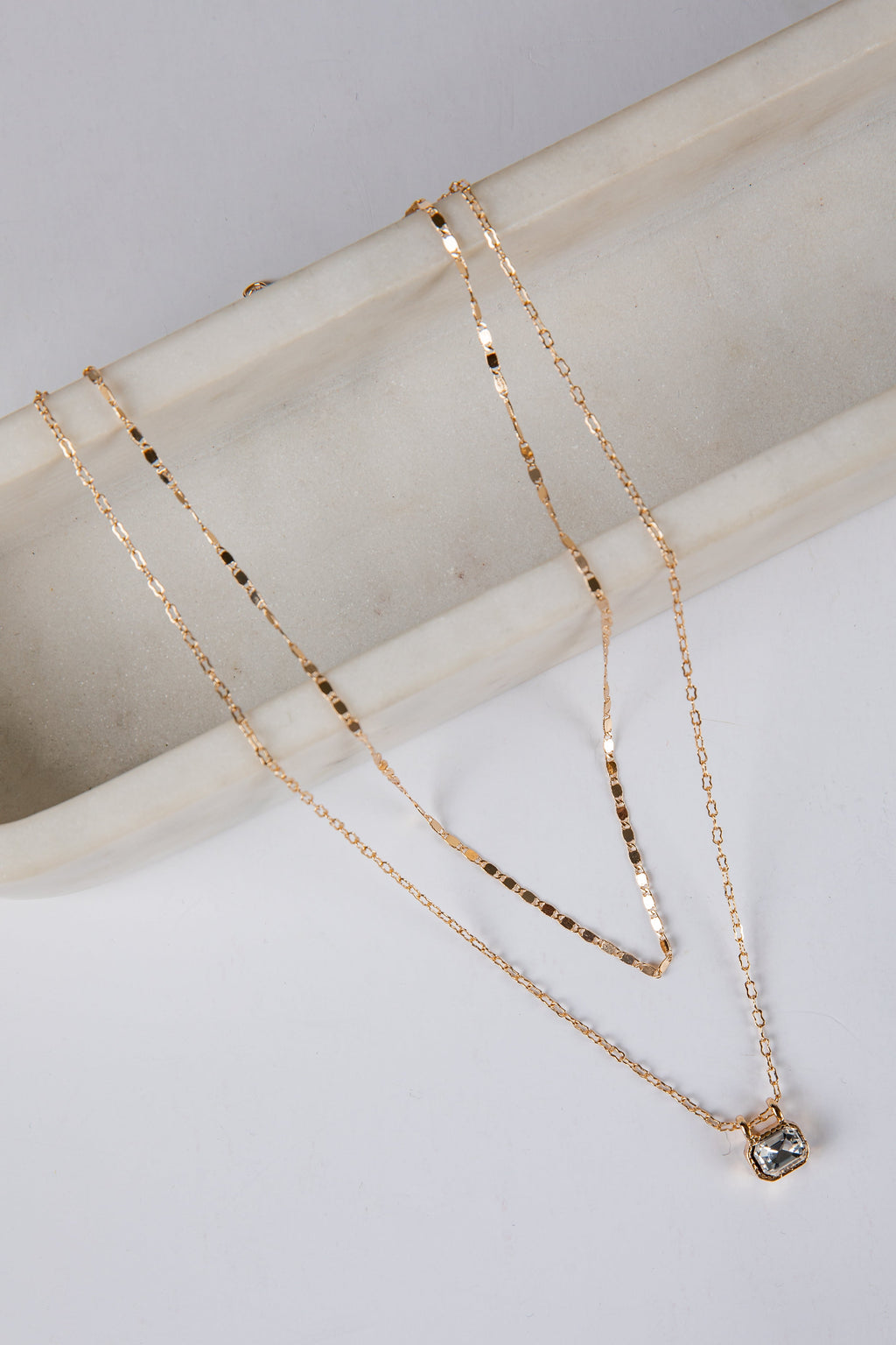 Two gold necklaces on a light gray surface